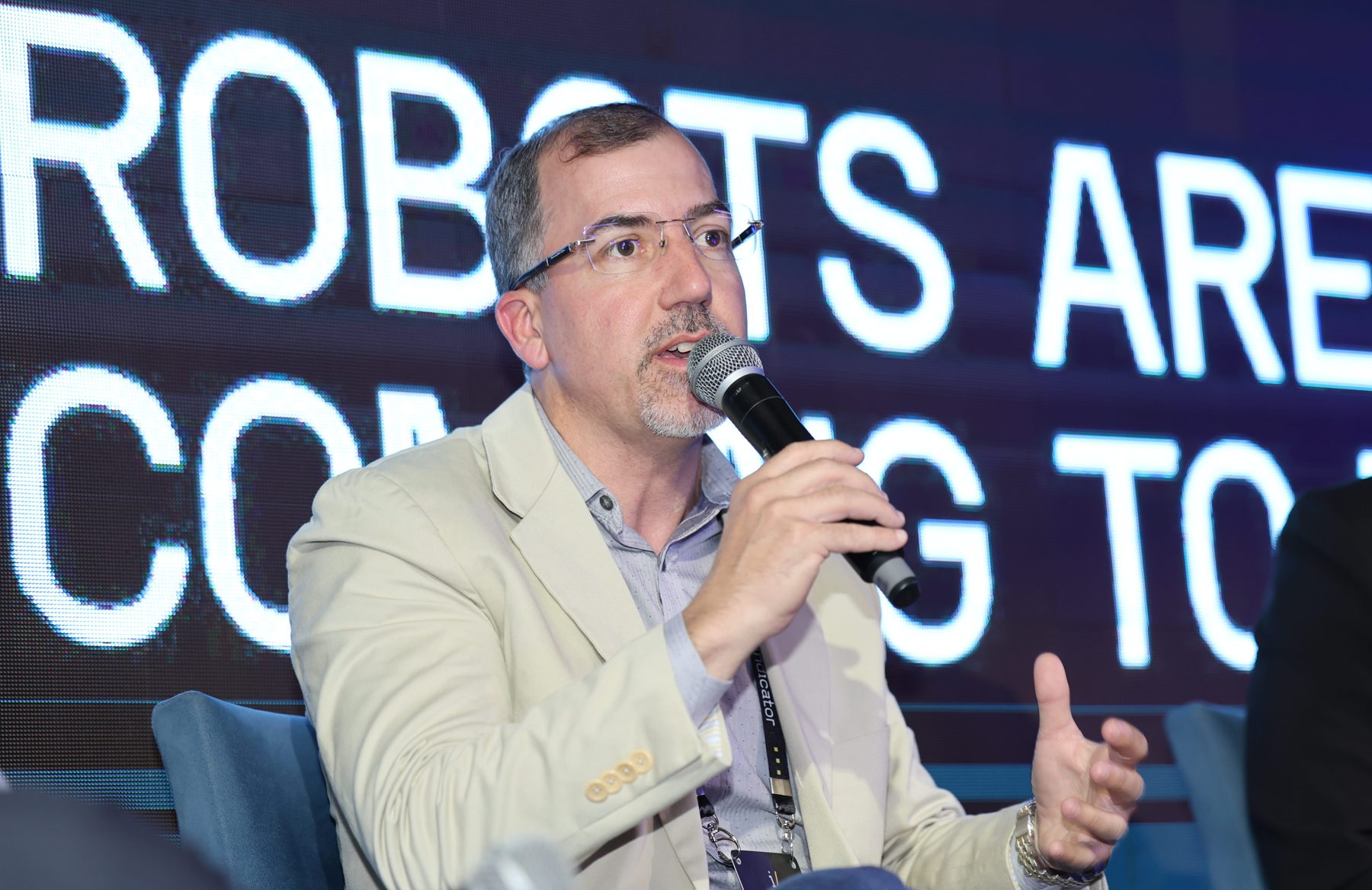 Marcel Gonçalves falando no palco diante do telão “Robots are Coming to Brazil” no Physical AI Summit